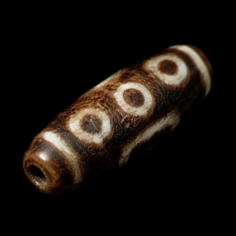 Authentic Tibetan Dzi agate bead with natural circular eye motifs resting on a dark background.
