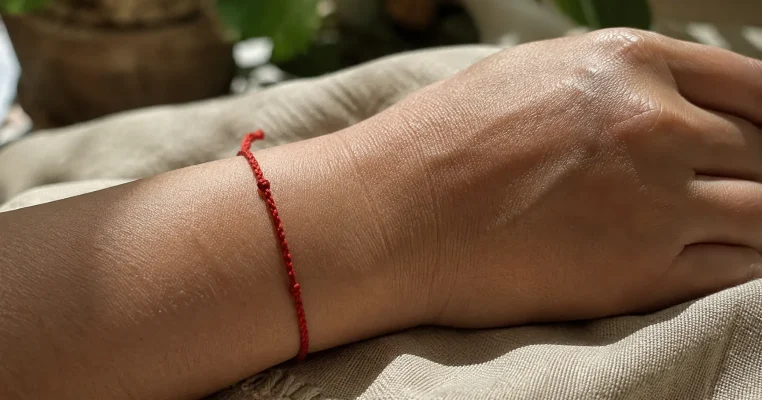 Close-up of a simple red string bracelet worn on a wrist resting on textured linen cloth in warm natural sunlight.