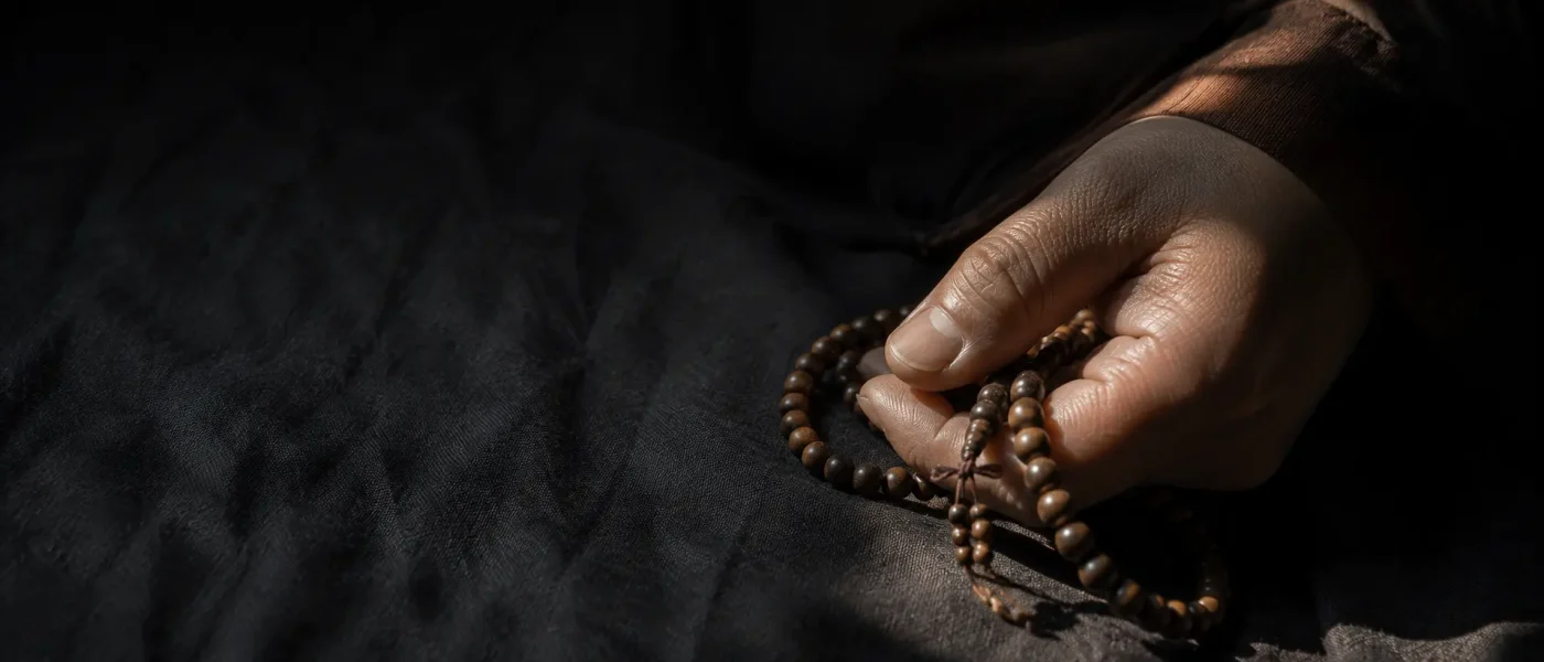 Close up of a hand gently holding wooden prayer beads on dark coarse linen in soft natural light, reflecting daily spiritual practice and mindfulness.
