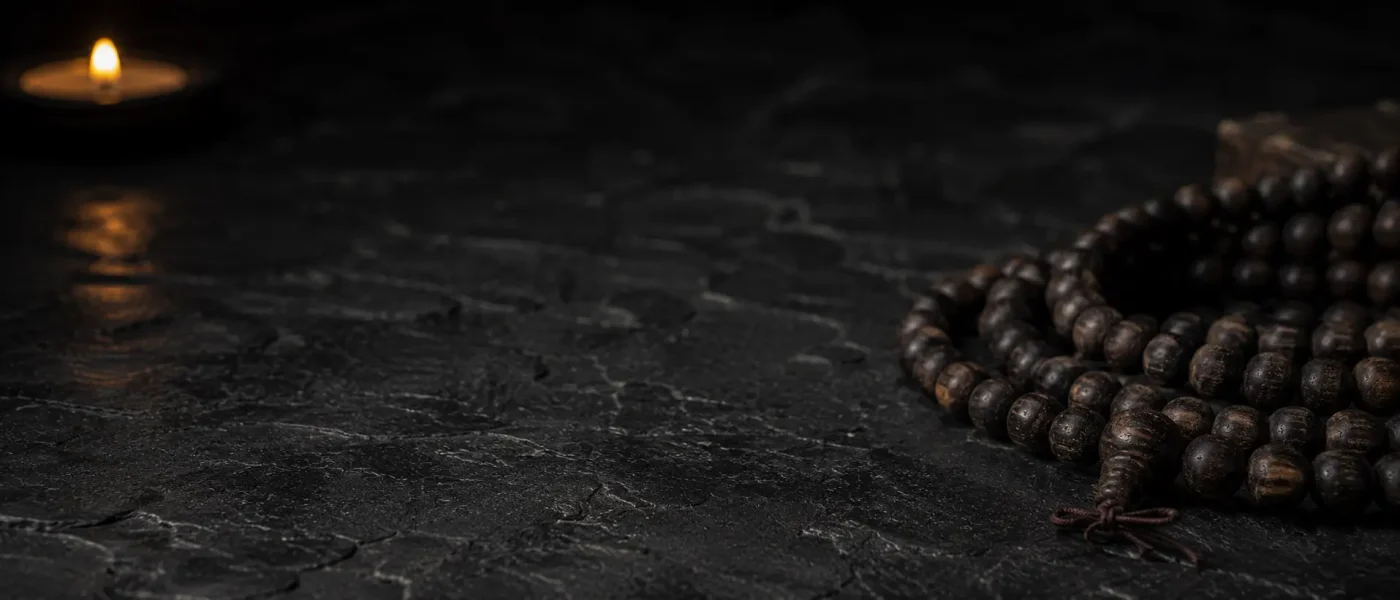 Traditional wooden mala beads resting on dark slate stone illuminated by soft candlelight, representing deep meditation and inner stillness.