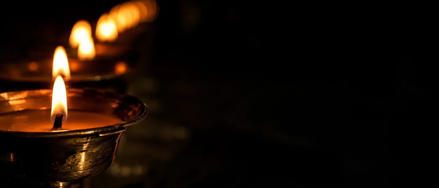 A row of glowing traditional brass butter lamps fading into dark shadow, symbolizing sacred offerings and spiritual devotion.